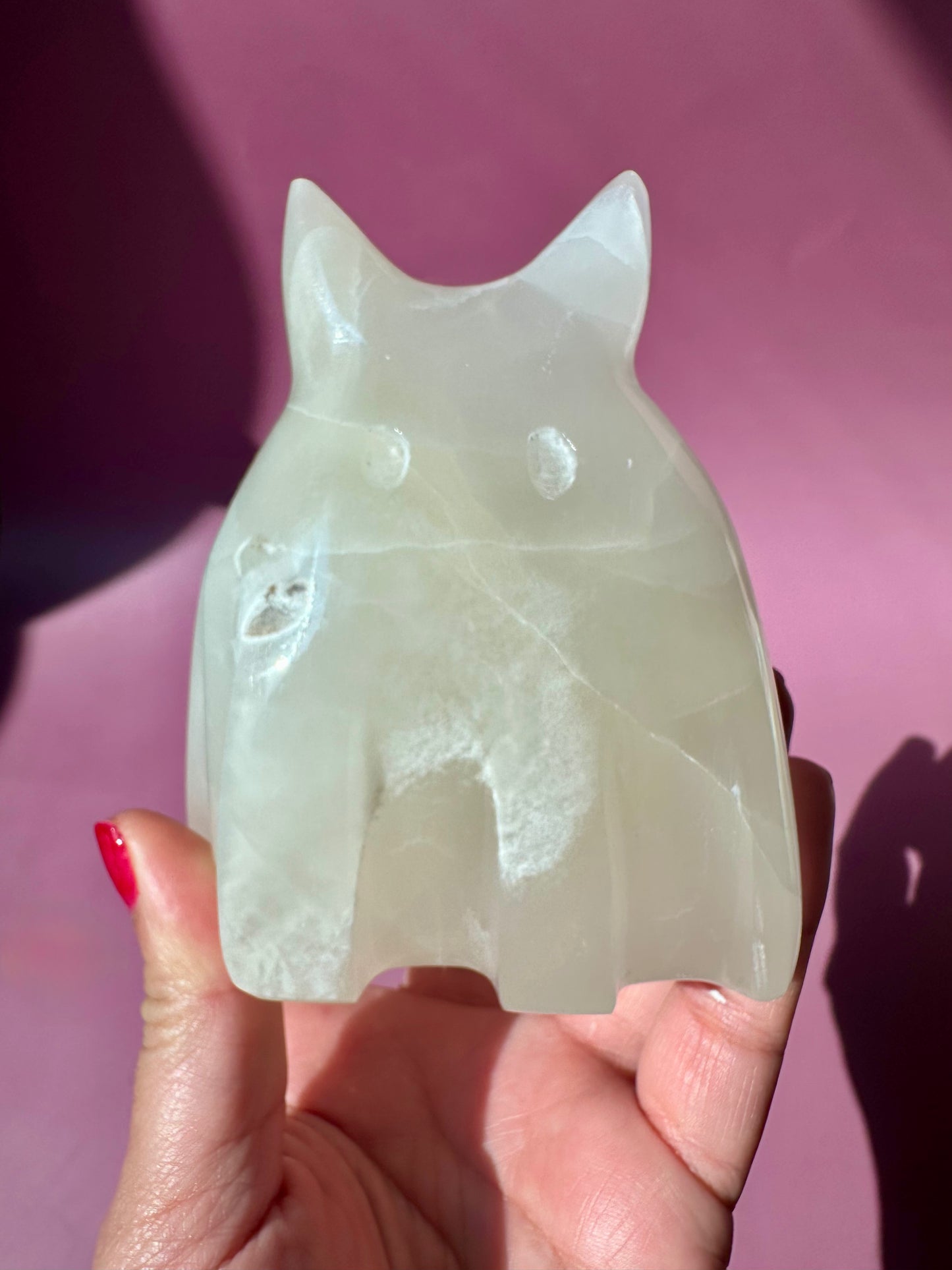 Hand holding a white stone object shaped like a cat against a pink background
