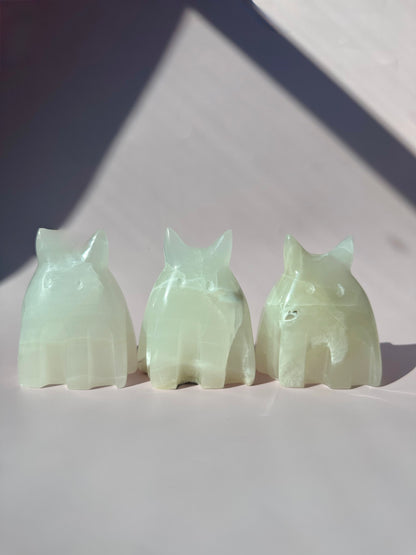Three jade cat figurines on a white surface with a gray background