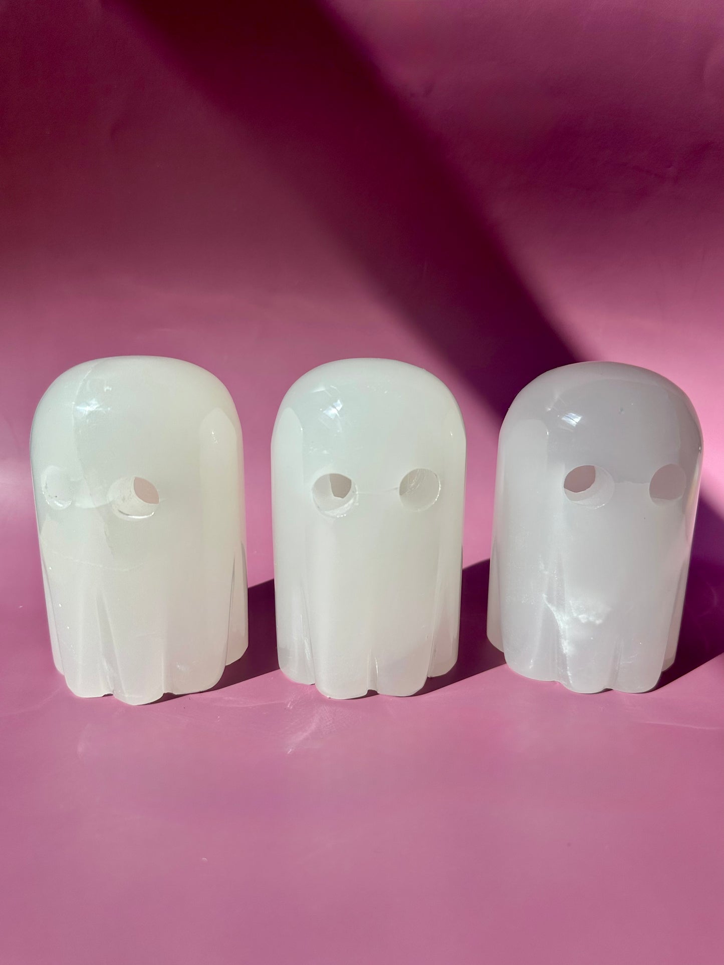 Three white ghost-shaped objects on a pink background

